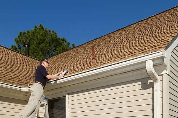 Inspector on a step ladder inspects a roof vent on a home.
